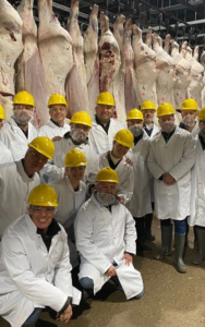 Grupo de invitados a la misión comercial en Canada, se encuentran en una planta de carne, todos vestidos con batas blancas, goggles y cascos amarillos