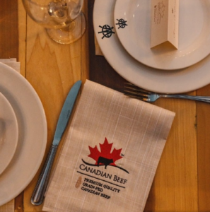 Foto mesa de la cena, enfocada a la servilleta de mano que tiene el logotipo de canada beef